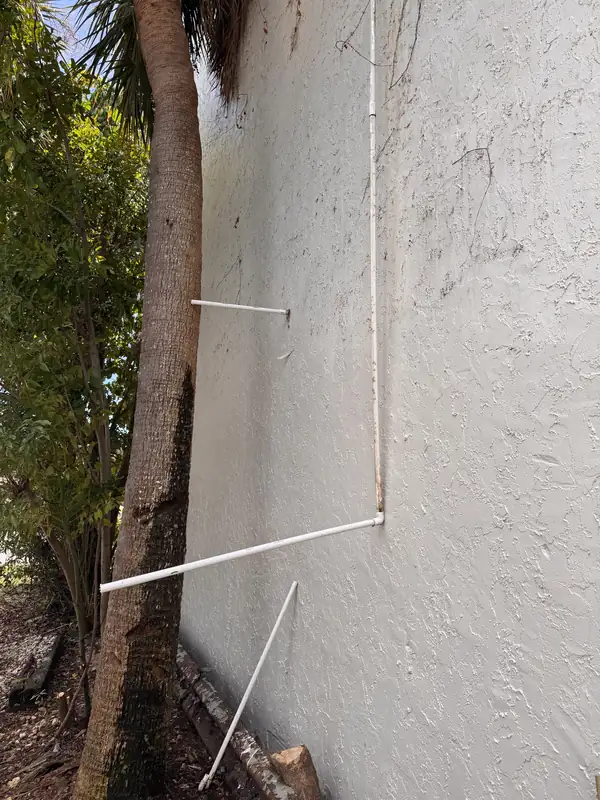 Pipes running along the exterior wall of a Sarasota building, broken near the ground