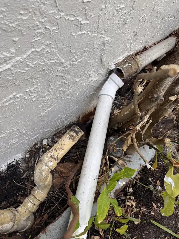 Broken pipes at the base of an exterior wall at a Sarasota property before repair